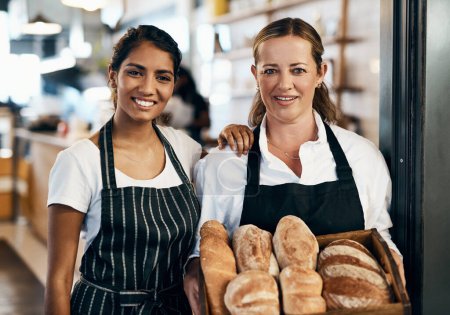 Téléchargez les photos : Choisis un pain, n'importe quel pain. deux femmes tenant une sélection de pains fraîchement cuits dans leur boulangerie - en image libre de droit