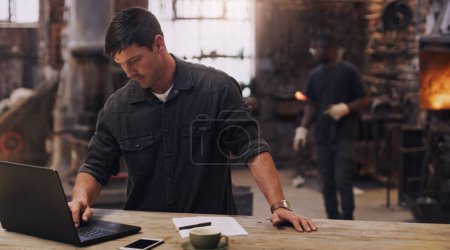 Photo for Workshop, man and working on laptop in metal blacksmith factory for trade business, finance and industry technology. Welder, computer and online paperwork for businessman, staff and forge worker. - Royalty Free Image