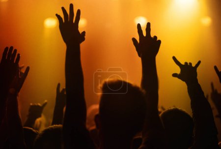 Téléchargez les photos : Lumières orange, mains de personnes au concert ou au festival de musique dansant avec énergie en silhouette lors d'un événement en direct. Danse, plaisir et groupe de fans excités dans l'arène à la performance du groupe de rock ou foule à la fête - en image libre de droit