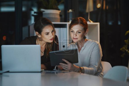 Photo for This app will make our job a lot easier. two businesswomen using a digital tablet together in an office at night - Royalty Free Image