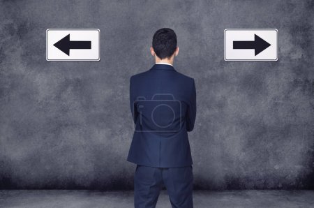 Photo for Back, arrow and direction with a business man planning or brainstorming a decision while in doubt on a wall background. Confused, challenge or strategy with a male employee thinking of a solution. - Royalty Free Image