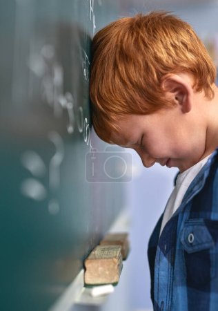 Foto de No le gusta no saber la respuesta. un niño de la escuela primaria presionando su cabeza contra la pizarra con frustración en clase - Imagen libre de derechos
