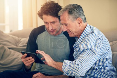 Téléchargez les photos : Surfe, fiston. un homme montrant à son père âgé comment utiliser une tablette à la maison - en image libre de droit