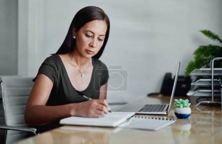 Photo for I better make a note of that. an attractive young businesswoman sitting and writing in a notebook while in the office alone - Royalty Free Image