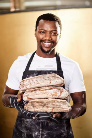 Téléchargez les photos : C'est célèbre parce que c'est bon. un boulanger mâle tenant du pain fraîchement cuit dans sa boulangerie - en image libre de droit