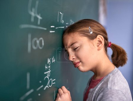 Photo for She doesnt like not figuring it out. an elementary school girl pressing her head against the blackboard with frustration in class - Royalty Free Image