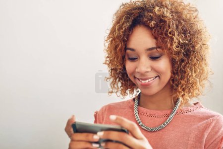 Photo for Its become so much easier to communicate with clients. a happy young designer using her smartphone while sitting at her desk in the office - Royalty Free Image