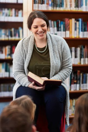 Foto de Leer a su clase le trae alegría. una maestra leyendo a niños de primaria en la biblioteca - Imagen libre de derechos
