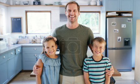 Foto de Estás mirando el contentamiento. Retrato recortado de un padre joven y cariñoso de pie con sus dos hijos en la cocina en casa - Imagen libre de derechos