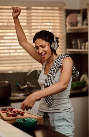 Téléchargez les photos : Écouteurs de musique, chant et cuisine femme à la fraise. Chantez, cuisinez et faites une collation avec des fruits pour une alimentation saine tout en dansant sur podcast audio, sonore et radio à la maison - en image libre de droit