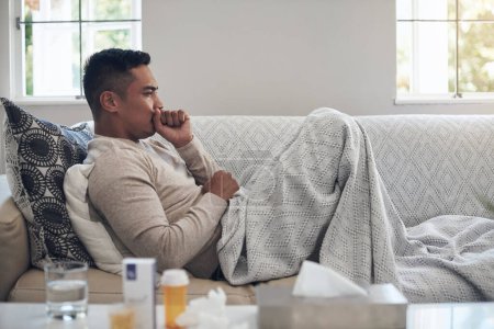 Foto de Sus síntomas están empeorando. un joven tosiendo mientras se siente enfermo en casa - Imagen libre de derechos