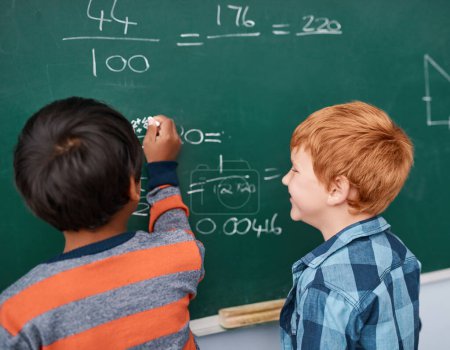 Photo for Wow youre really good at this. two focussed young elementary school kids writing answers to math questions on a green chalkboard in the classroom - Royalty Free Image