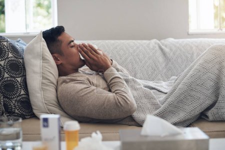 Foto de Llegó la temporada de gripe. un joven sonándose la nariz mientras se siente enfermo en casa - Imagen libre de derechos