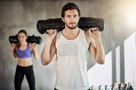 Foto de Hacer músculos, no excusas. dos jóvenes haciendo ejercicio en el gimnasio usando bolsas pesadas - Imagen libre de derechos