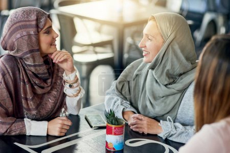 Foto de Sonríe, amigos y mujeres musulmanas en la cafetería, vinculándose y hablando juntos. Café, relax y chicas islámicas, chat grupal o de personas, conversación y discusión para reunión social en restaurante - Imagen libre de derechos