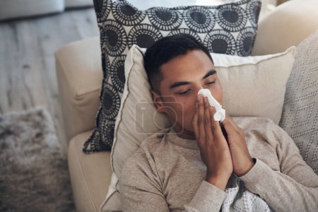Photo for Looks like Im going to go through many tissues today. a young man blowing his nose while feeling sick at home - Royalty Free Image