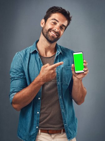 Foto de Hombre feliz, teléfono y apuntando a la pantalla verde maqueta para la publicidad contra un fondo gris estudio. Retrato de persona masculina sonriendo y mostrando la pantalla del teléfono inteligente o cromakey para publicidad. - Imagen libre de derechos
