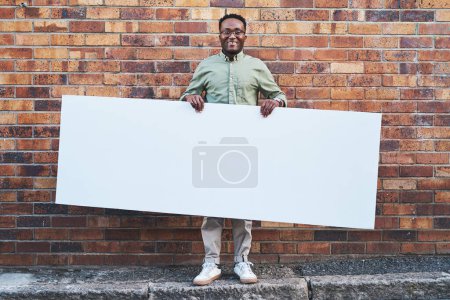Foto de Tengo la señal perfecta para ti. un joven sosteniendo una pancarta en blanco sobre un fondo urbano al aire libre - Imagen libre de derechos