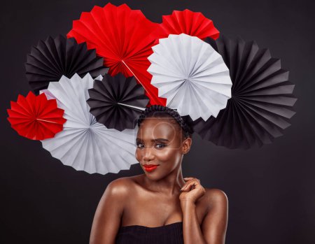Téléchargez les photos : Portrait, soin de la peau et femme noire avec des fans d'origami en studio isolé sur un fond sombre. Visage, maquillage et beauté du modèle féminin africain avec chapeau traditionnel japonais en papier pour la mode. - en image libre de droit