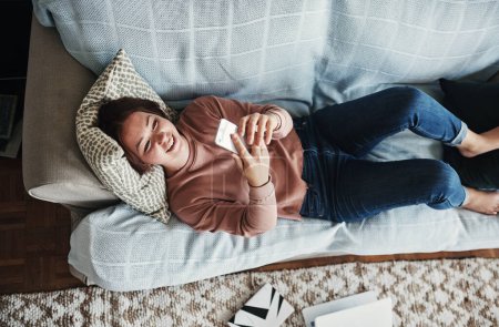 Photo for I never want to leave this couch. High angle shot of an attractive young woman lying on her home sofa alone and texting on her cellphone - Royalty Free Image