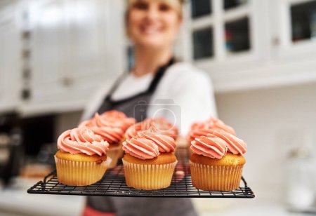 Téléchargez les photos : Il y a toujours un marché pour les produits de boulangerie délicieux. une femme tenant des cupcakes fraîchement cuits dans sa cuisine à la maison - en image libre de droit