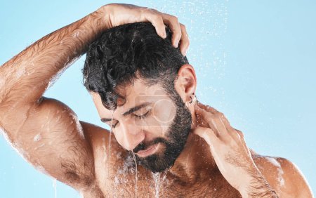 Foto de Hair care, face and water splash of man in shower in studio isolated on a blue background. Water drops, dermatology and male model washing, cleaning or bathing for skincare, wellness and hygiene - Imagen libre de derechos