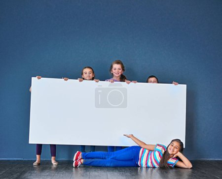 Photo for An important message brought to you by the kids. Studio shot of a diverse group of kids standing behind a large blank banner against a blue background - Royalty Free Image