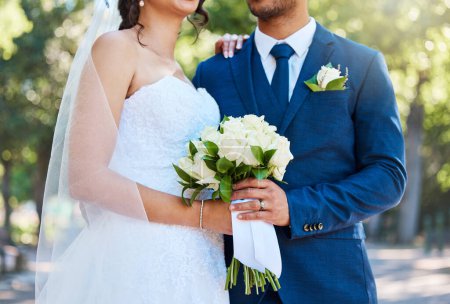 Foto de Close up of a bride in her wedding dress and groom in suit holding on to a bouquet while standing together on their wedding day. Couple tying the knot. Wedding detail. - Imagen libre de derechos