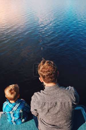 Téléchargez les photos : La pêche est une tradition le dimanche. un père et son jeune fils à la pêche au bord du lac - en image libre de droit