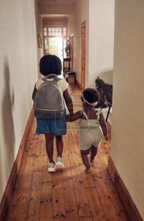 Photo for Off to school we go. Rearview shot of a young school girl walking with her baby sister through the passage at home - Royalty Free Image
