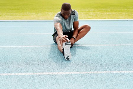 Photo for Feel the burn. Full length shot of an unrecognizable athlete sitting alone and stretching before a run on the track - Royalty Free Image