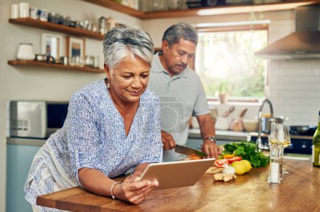 Photo for Senior woman at kitchen counter with man, tablet and cooking healthy food together in home. Digital recipe, smile and old couple in house with meal prep, happiness and wellness diet in retirement - Royalty Free Image