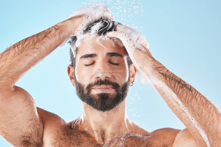 Foto de Hair care, face water splash and shower of man in studio isolated on a blue background. Water drops, shampoo and male model washing, cleaning or bathing for healthy skin, wellness or skincare hygiene. - Imagen libre de derechos