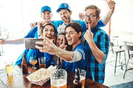 Téléchargez les photos : Journée de jeu en plein effet. un groupe d'amis prenant un selfie tout en regardant un jeu de sport dans un bar - en image libre de droit