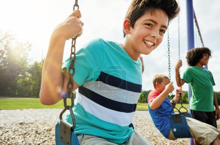 Téléchargez les photos : Le cadeau essentiel pour un enfant est le temps de jouer. jeunes garçons jouant sur les balançoires au parc - en image libre de droit