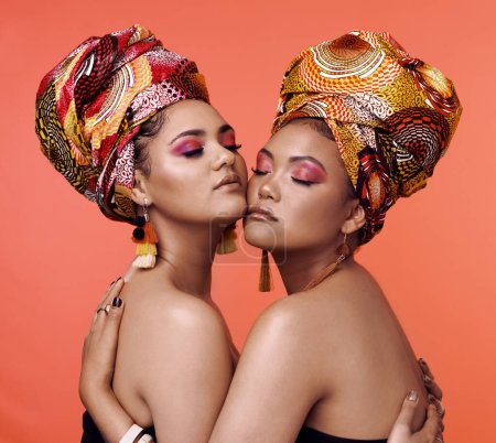 Téléchargez les photos : Mode, beauté et femmes africaines s'embrassent sur fond orange avec cosmétiques, maquillage et accessoires. Glamour, luxe et femmes avec bijoux exotiques, style traditionnel et foulard en studio. - en image libre de droit