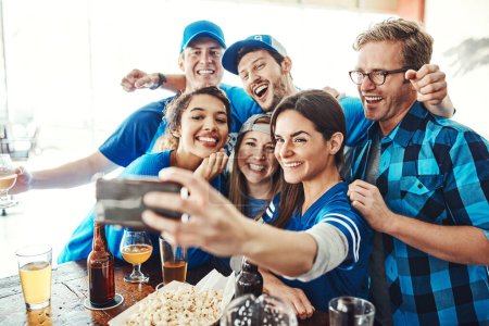 Téléchargez les photos : Coup d'envoi du jeu avec un selfie. un groupe d'amis prenant un selfie tout en regardant un jeu de sport dans un bar - en image libre de droit