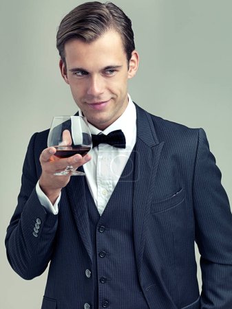 Photo for Hes on the prowl. A studio shot of a dapper young man holding a glass of red wine and looking mischievous - Royalty Free Image