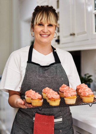 Photo for Start selling your baked goods from home. a woman holding freshly baked cupcakes in her kitchen at home - Royalty Free Image