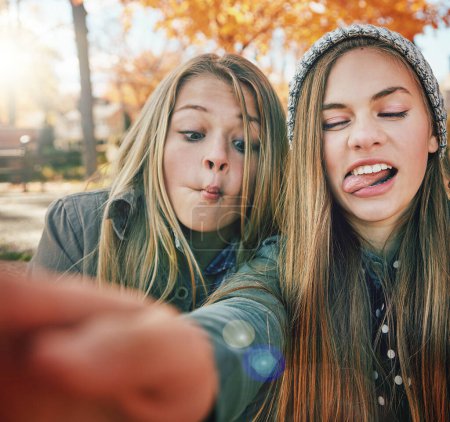 Téléchargez les photos : Les amis sont les gens avec qui on peut être fou. deux jeunes amis tirant des visages drôles tout en posant pour un selfie ensemble à l'extérieur - en image libre de droit