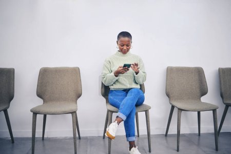 Photo for Black woman, phone and sitting on a chair in a waiting room with internet connection for social media. African female person in line for recruitment interview with a smartphone for communication app. - Royalty Free Image