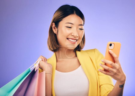 Foto de Mujer asiática, selfie y bolsa de compras en estudio con sonrisa para trato, venta o descuento por telón de fondo. Chica influencer japonesa, minorista y feliz con las redes sociales, contacto y lujo por fondo púrpura. - Imagen libre de derechos