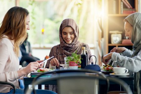 Téléchargez les photos : Femmes musulmanes, amis et manger au restaurant, ensemble et parler avec la nourriture, sourire ou le bonheur. Femme islamique, groupe et brunch avec conversation, visage heureux ou écoute avec le chat social dans le café. - en image libre de droit