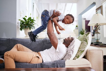 Photo for Black family, airplane and father with son on a sofa with love, lifting and playing in their home together. Flying, child and fun with parent on sofa, laugh and play, bonding and games in living room. - Royalty Free Image