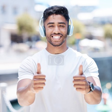 Photo for Happy man, headphones and listening to music with thumbs up for winning, fitness or success in city. Portrait of male person, athlete or runner with headset, thumb emoji or yes sign for audio track. - Royalty Free Image