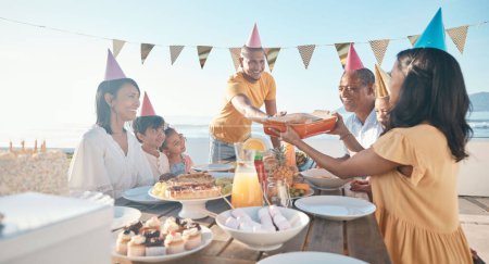 Photo for Birthday, parents and children with food by beach for event, celebration and party outdoors. Family, social gathering and mother, father with kids at picnic with cake, presents and eating together. - Royalty Free Image