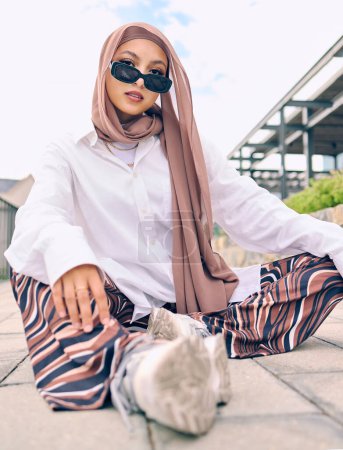 Foto de Retrato, moda o tradición con una mujer musulmana al aire libre en gafas de sol y una bufanda de estilo contemporáneo. Islam, fe o hiyab con una persona islámica joven de moda sentada fuera con ropa moderna. - Imagen libre de derechos