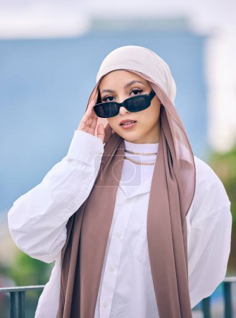 Téléchargez les photos : Portrait, mode ou lunettes de soleil avec une femme musulmane en dubai portant un bonnet et une écharpe pour un style contemporain. Islamique, foi et hijab avec un jeune arabe branché posant dehors dans des lunettes modernes. - en image libre de droit