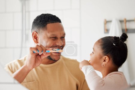 Foto de Padre, hijo y cepillarse los dientes en un cuarto de baño familiar para la salud dental y el bienestar en un espejo. Hombre y niña africanos felices aprendiendo a limpiar la boca con un cepillo de dientes para la higiene bucal. - Imagen libre de derechos