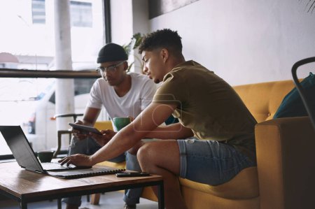 Foto de Haciendo que las cosas sucedan durante el café. dos jóvenes discutiendo algo en un portátil mientras están sentados juntos en un café - Imagen libre de derechos